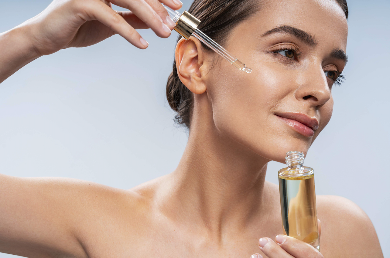 Model holds a bottle of serum and applies a few drops on her cheek